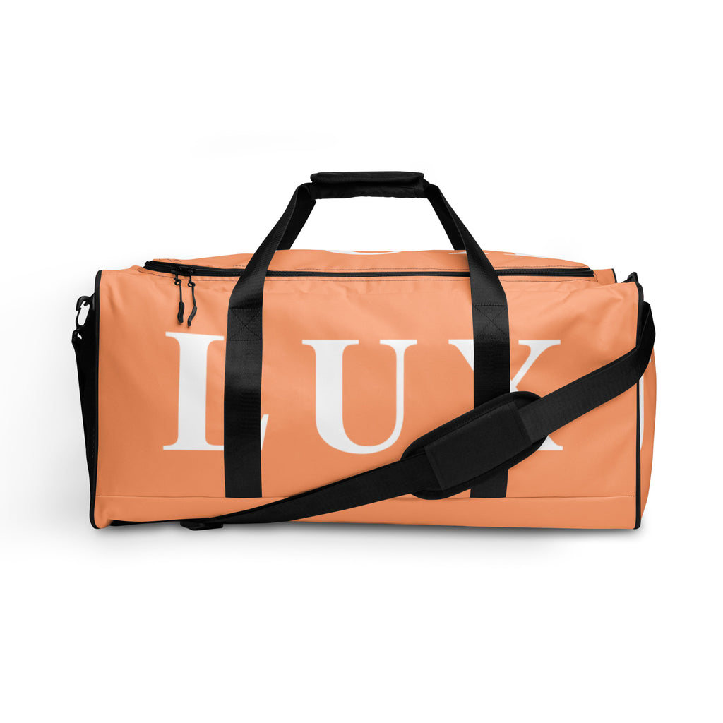 A light salmon (pink) duffle bag with black handles and a black shoulder strap, featuring the word 'LUX' prominently displayed on the side.